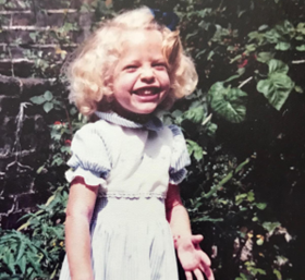 Anna Balcombe as a young child with curly blonde hair in a garden
